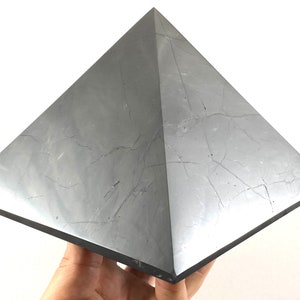 Puede incluir: Un gran cristal gris en forma de pirámide con una superficie lisa y pulida. El cristal tiene un patrón natural de mármol.