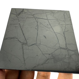 Puede incluir: Una pieza cuadrada de obsidiana negra con un patrón natural veteado. La obsidiana es lisa y pulida.