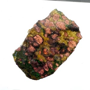 Könnte beinhalten: Ein Naturstein-Exemplar mit einer Mischung aus Farben. Der Stein weist eine Basis aus gelben und grünen Farbtönen mit rotbraunen kreisförmigen Mustern auf. Die Kanten sind rau und unregelmäßig, was ihm ein rohes, organisches Aussehen verleiht.