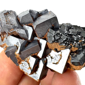 May include: A cluster of gray and black pyrite crystals with a metallic sheen. The crystals are sharp and well-defined, and they are arranged in a random pattern. The crystals are set against a white background.