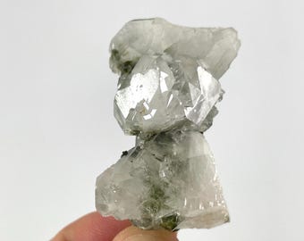 May include: A cluster of clear quartz crystals with a layered structure. The crystals have sharp, geometric facets and exhibit a translucent quality. Some areas show hints of green inclusions, adding subtle color variations.