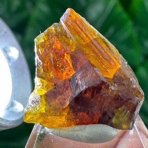 Peut inclure: Gros plan sur une formation cristalline naturelle brute. Le cristal présente une gamme de couleurs, dont l'ambre, l'orange et le marron. Le cristal est éclairé par une source de lumière vive, soulignant sa surface texturée et sa structure interne. L'arrière-plan est vert flou.