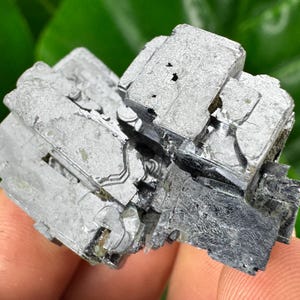 May include: A cluster of gray and black metallic mineral crystals with a layered, geometric structure.
