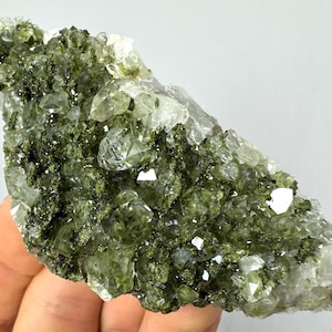 Op de afbeelding: Een cluster van heldere kwartskristallen met groene epidote-insluitsels. De kristallen zijn in een ruwe, natuurlijke formatie geclusterd.