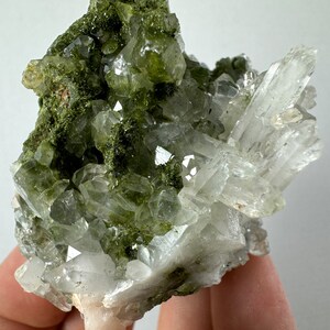 May include: A cluster of clear quartz crystals with green epidote inclusions. The crystals are arranged in a random pattern and have a natural, rough texture.