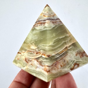 Peut inclure: Objet décoratif en forme de pyramide, en onyx vert. Le motif naturel de la pierre présente des nuances de blanc, marron et beige, créant un effet de couches. L'objet est présenté sur fond blanc.