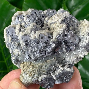 May include: A close-up of a mineral specimen featuring a cluster of metallic gray galena crystals with white quartz and a tan matrix. The crystals have a reflective surface and are surrounded by smaller, sparkling quartz formations.