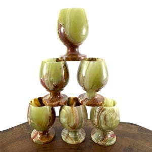 Puede incluir: Juego de seis vasos de chupito de ónix verde y marrón apilados en forma de pirámide sobre una superficie de madera.