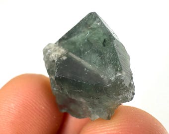 May include: A green fluorite crystal with a sharp, faceted shape. The crystal has a translucent appearance and shows some internal striations.