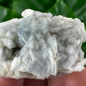 Può includere: Primo piano di un campione minerale azzurro e bianco. Il minerale ha una struttura cristallina con una superficie ruvida e strutturata. Il colore è un mix di azzurro e bianco, con alcune aree traslucide.