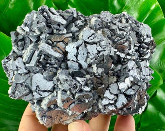May include: A large cluster of gray and silver metallic crystals with a rough, textured surface. The crystals are tightly packed together, forming a dense, solid mass.