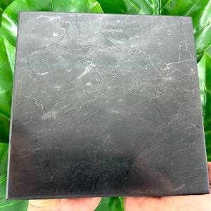 May include: A black square slab of polished obsidian with a marbled pattern. The obsidian is a dark gray with white veins running through it.