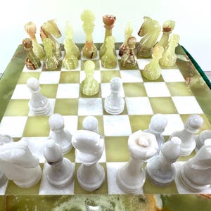 Könnte beinhalten: Ein Schachspiel mit einem Brett aus abwechselnd hellgrünen und weißen Feldern. Die Figuren sind aus Stein geschnitzt, wobei ein Satz in durchscheinendem Hellgrün und der andere in undurchsichtigem Weiß gehalten ist, inklusive Königen, Damen, Läufern, Springern, Türmen und Bauern.