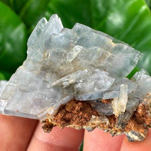 May include: A cluster of blue barite crystals on a matrix of brown rock. The crystals are translucent and have a layered structure.