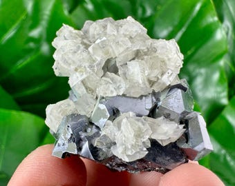 May include: A close-up of a mineral specimen featuring clear, crystalline formations atop a dark, metallic base. The crystals are translucent, and the base has a reflective, geometric structure. The background is a vibrant green.