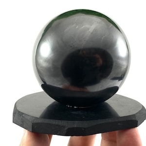 May include: A large, polished black obsidian sphere resting on a black obsidian base. The sphere is smooth and reflective, with a slight sheen.