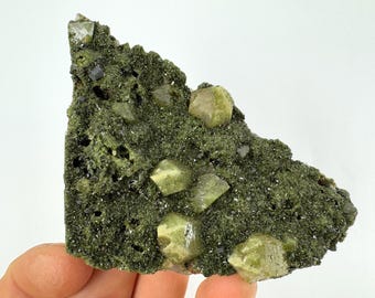 May include: A cluster of green and yellow crystals on a dark green matrix. The crystals are sharp and well-defined, with a glassy luster. The matrix is rough and textured.