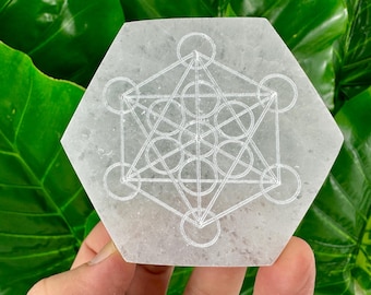 May include: White selenite charging plate with a carved flower of life geometric design. The plate is hexagonal in shape.