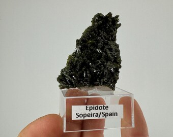 May include: A dark green epidote crystal cluster on a clear display stand with a label that reads "Epidote Sopeira/Spain".