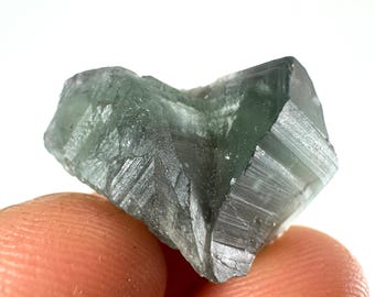May include: A green fluorite crystal with a striated surface. The crystal is translucent and has a light green color.