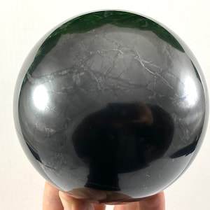 Peut inclure: Une grande sphère d'obsidienne noire polie avec une finition très brillante. La sphère présente un motif naturel marbré sur toute sa surface.