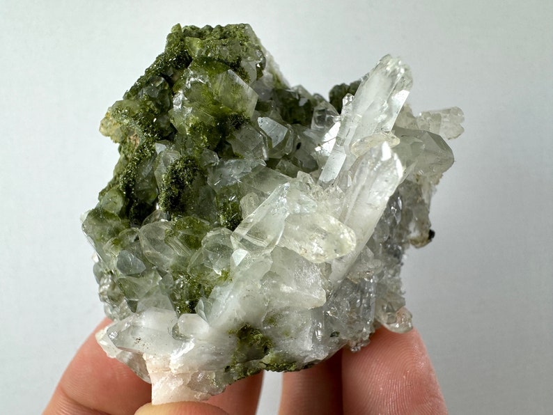 May include: A cluster of clear quartz crystals with green epidote inclusions. The crystals are clustered together in a natural formation.