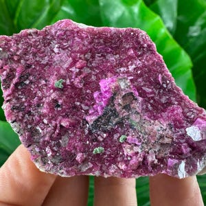 May include: A pink and purple calcite crystal cluster with a rough, natural texture. The crystal is a vibrant shade of pink with hints of purple and green.