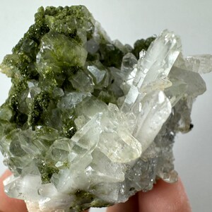 May include: A cluster of clear quartz crystals with green epidote inclusions. The quartz crystals are sharp and well-formed, and the epidote is a deep green color.