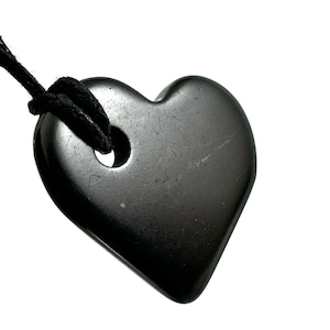 Puede incluir: Un colgante negro en forma de corazón hecho de piedra pulida, colgado de un cordón negro.