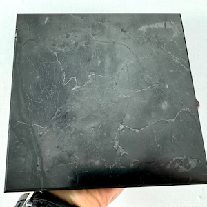 May include: A square black tile with a marbled pattern. The tile has a smooth, polished surface.