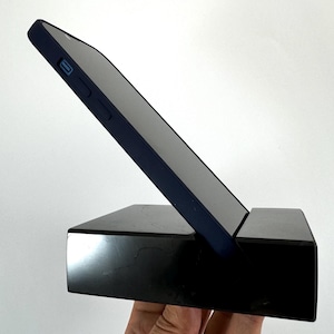 Könnte beinhalten: Ein schwarzer Telefonständer mit einem marineblauen Telefon. Der Ständer ist rechteckig mit einem Schlitz, um das Telefon in einem Winkel zu halten. Das Telefon hat eine marineblaue Hülle.