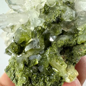 May include: A cluster of clear quartz crystals with green epidote inclusions. The crystals are clustered together in a natural formation.