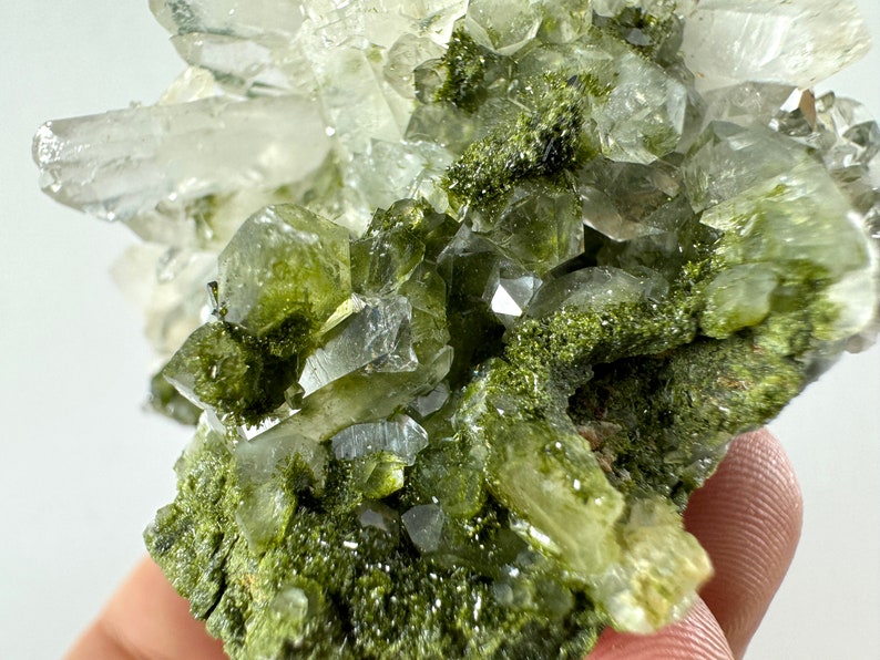 May include: A cluster of clear quartz crystals with green epidote inclusions. The crystals are clustered together in a natural formation.