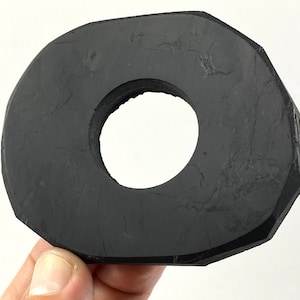 Könnte beinhalten: Ein schwarzer, ovaler Steinring mit einem Loch in der Mitte. Der Ring hat eine raue, strukturierte Oberfläche.