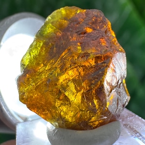 Peut inclure: Une pierre précieuse brute et translucide avec une forme irrégulière à facettes. La pierre présente un dégradé de couleurs éclatant, passant d'un jaune vif et lumineux au sommet à une teinte ambre profonde et orange brûlé vers la base.