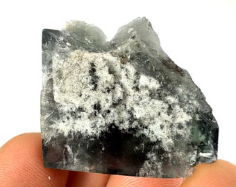 May include: A large, dark green fluorite crystal with white inclusions. The crystal has a rough, natural surface and is translucent.