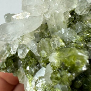 May include: Cluster of clear quartz crystals with green inclusions. The crystals are clustered together in a natural formation.