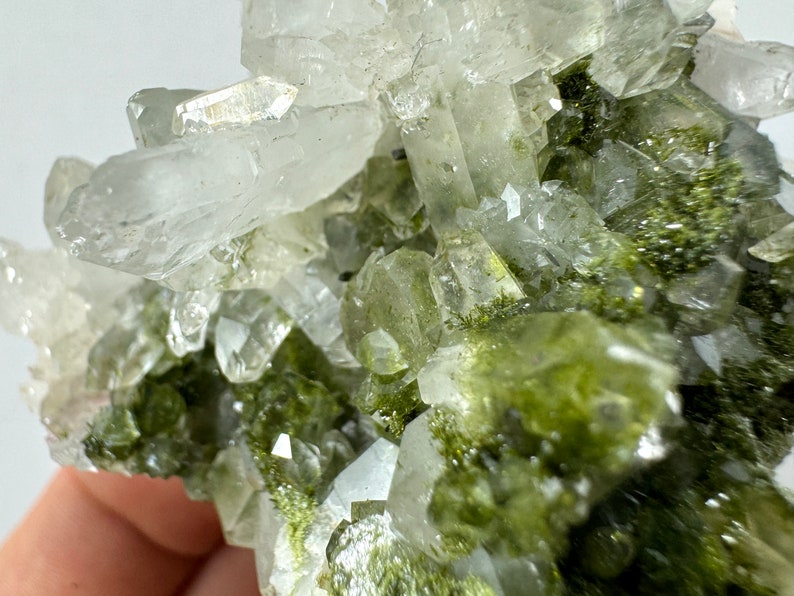 May include: Cluster of clear quartz crystals with green inclusions. The crystals are clustered together in a natural formation.