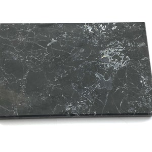 May include: A black marble tile with white veining. The tile is rectangular and has a smooth, polished surface.