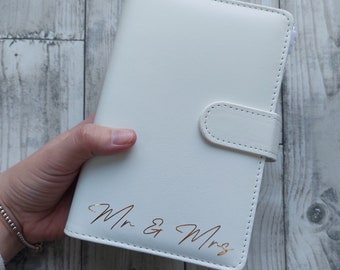 May include: White leather planner with a gold inscription that reads "Mr & Mrs".