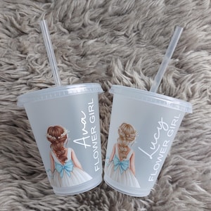 May include: Two clear plastic cups with lids and straws. Each cup has a drawing of a girl in a white dress with a blue bow. The text "Ava FLOWER GIRL" and "Lucy FLOWER GIRL" are printed on the cups.