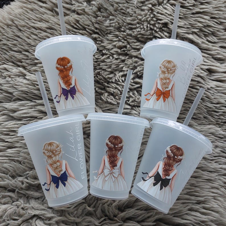 May include: Five clear plastic tumblers with lids and straws. Each tumbler features a drawing of a girl in a white dress with a bow. The text "Flower Girl" and a name are printed on the side.