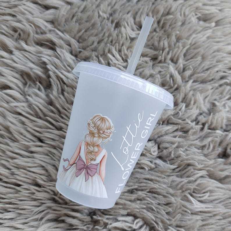 May include: A clear plastic cup with a lid and straw. The cup features a graphic of a girl in a white dress with a pink bow. The text "Lottie Flower Girl" is printed on the side of the cup.