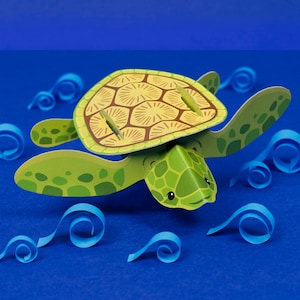 Puede incluir: Una tortuga de mar de papel verde y amarilla con un caparazón estampado nada a través de olas de papel azules.