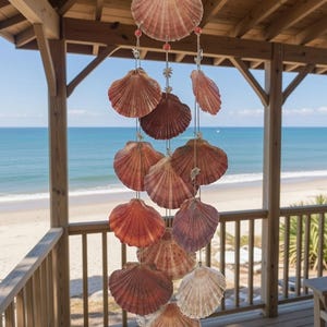 May include: A decorative mobile made of scallop shells in shades of orange, brown, and cream. The shells are suspended from a string with small beads. The background shows a beach and the sea.
