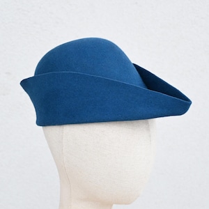 May include: A blue felt hat with a curved brim and a rounded crown. The hat is displayed on a mannequin head against a white background. The hat's color is a deep, saturated blue.