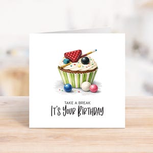 May include: A birthday card featuring a cupcake design with a pool theme. The cupcake has a green and white striped wrapper, white frosting, and is topped with a pool table triangle, balls, and a cue. The text reads "Take a break, It's Your Birthday."