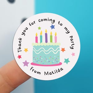 May include: A round sticker with a light blue cake illustration, topped with five candles. The text reads "Thank you for coming to my party" and "From Matilda". Colorful stars and sprinkles decorate the sticker.