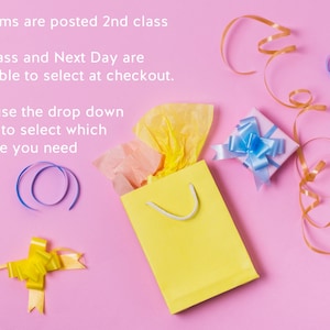 May include: A yellow gift bag with white handle, tissue paper, and a small gift box with a blue bow on a pink background. Gold and blue ribbons and a yellow bow are also present.