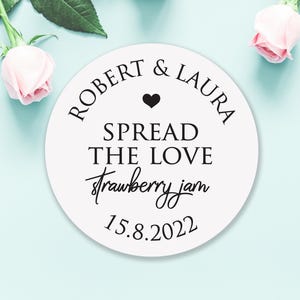 May include: White round sticker with black text that reads "Robert & Laura Spread the Love strawberry jam 15.8.2022". A small black heart is above the text "Spread the Love".